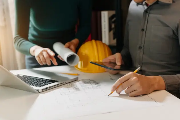 Zwei Kollegen diskutieren über Datenarbeit und Tablet, Laptop mit auf einem architektonischen Projekt auf der Baustelle am Schreibtisch im Büro